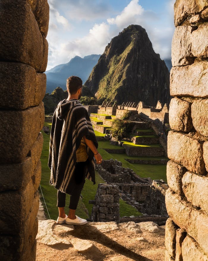 services-03 A man in traditional clothing overlooks the ancient ruins of Machu Picchu during daytime.