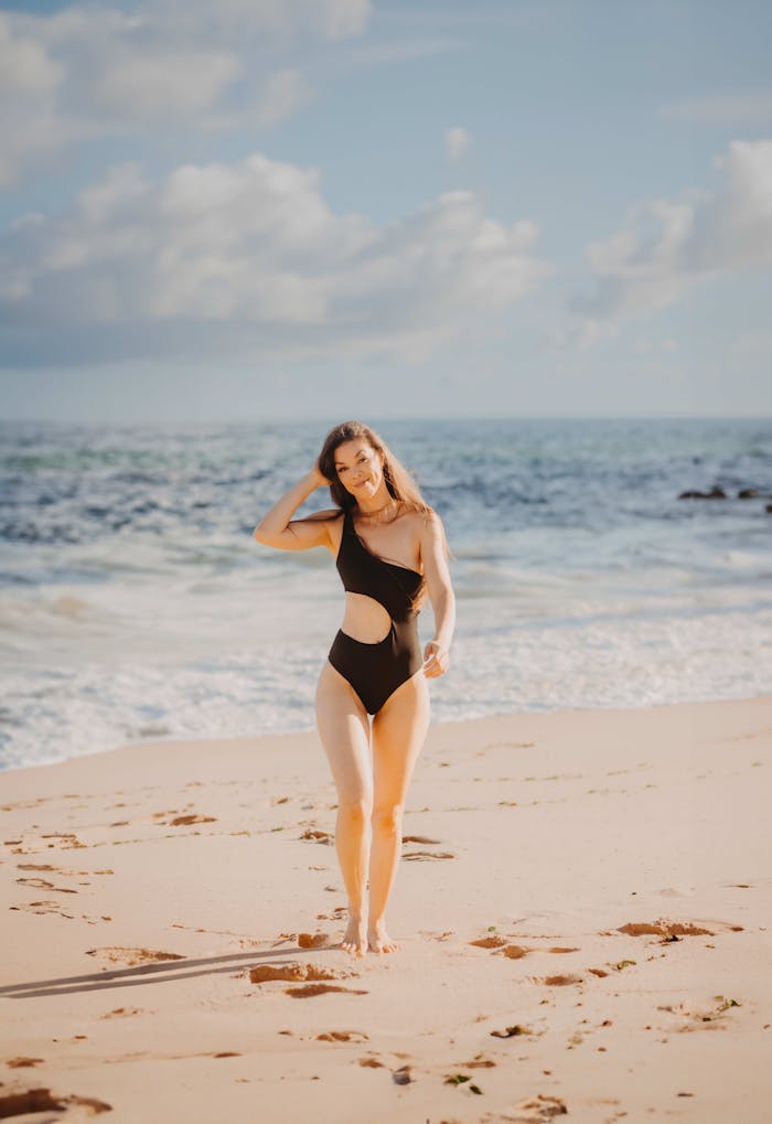 services-04 A woman enjoying a sunny day walking on a sandy beach in a black swimsuit.