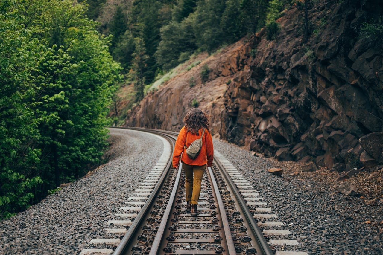 services-img-01 A woman walking on a railroad track through scenic nature in Northern California, embracing freedom and adventure.