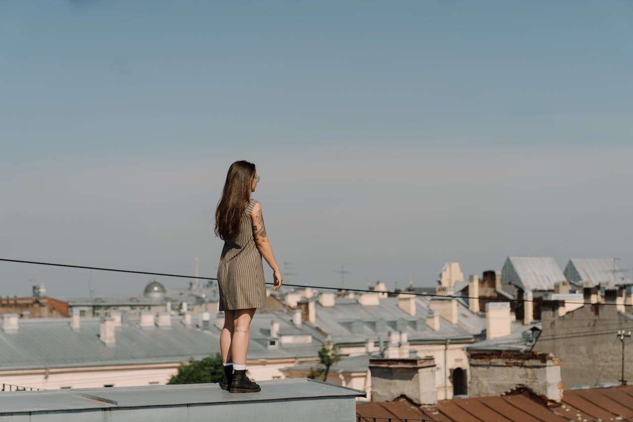 services-01 A woman stands on a rooftop, gazing over an urban cityscape under a clear blue sky.