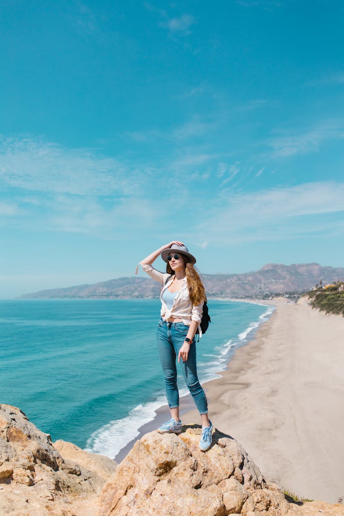 Woman standing on a bluff overlooking a beautiful beach and ocean in sunny weather.
