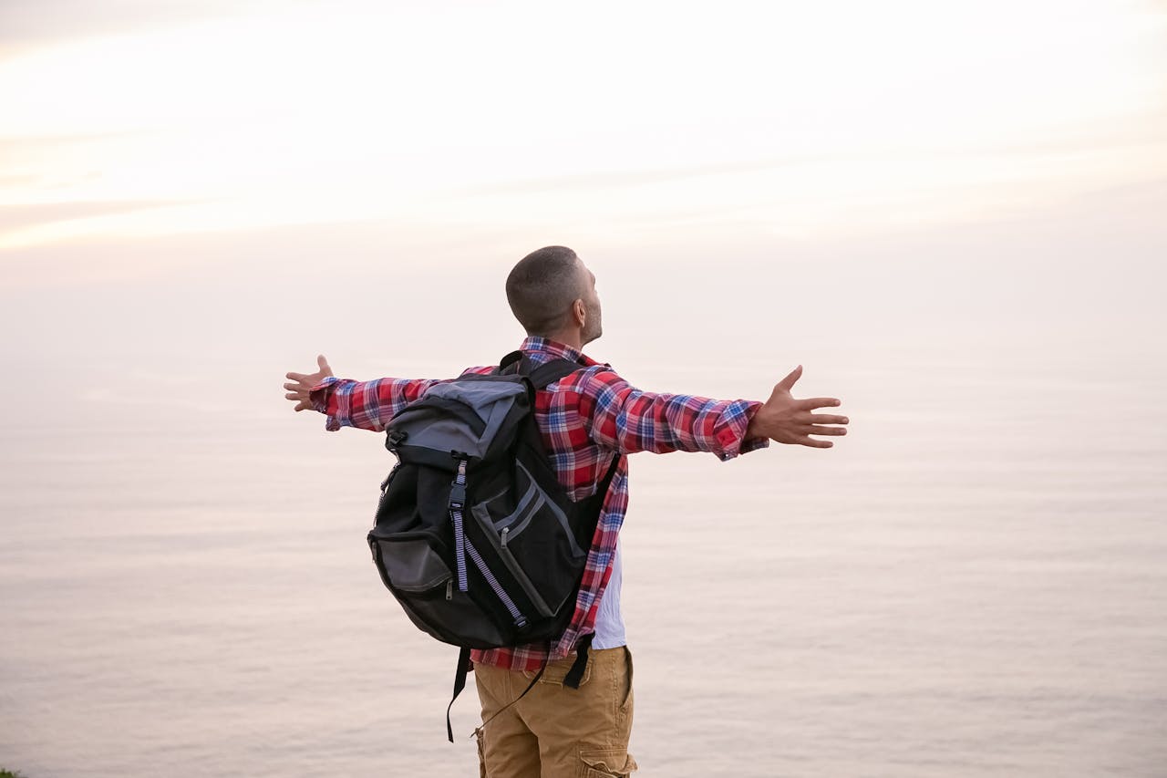 services-img-02 A man in plaid exploring a scenic ocean view with arms outstretched in a sense of freedom.